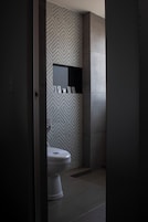 A modern bathroom with a geometric patterned wall, a white toilet, and a small shelf with toiletries.