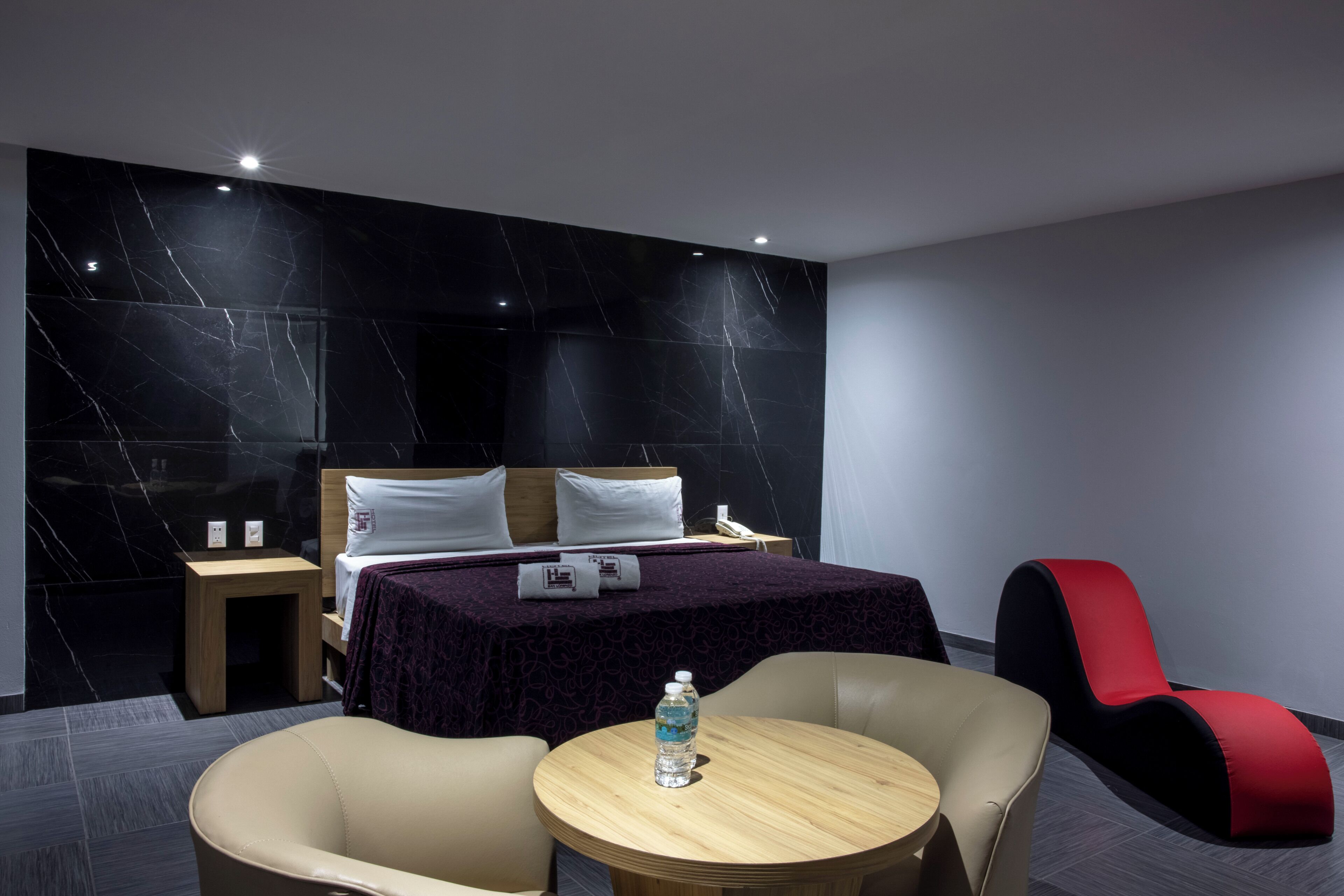 Una habitación de hotel moderna con una cama, dos sillas, una mesita pequeña y un sillón rojo.