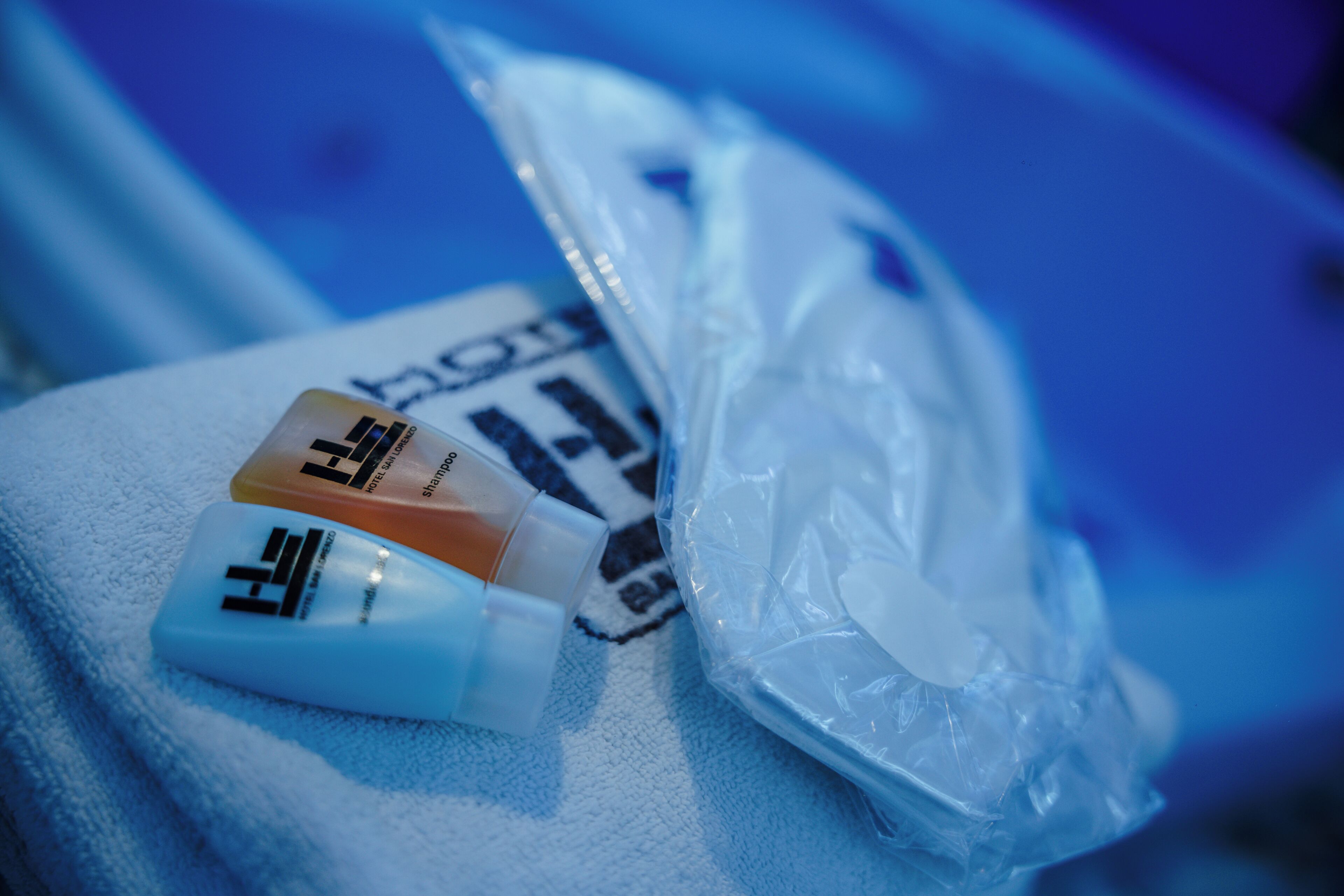 Una bolsa de plástico con artículos de aseo personal y una toalla blanca sobre una superficie azul.