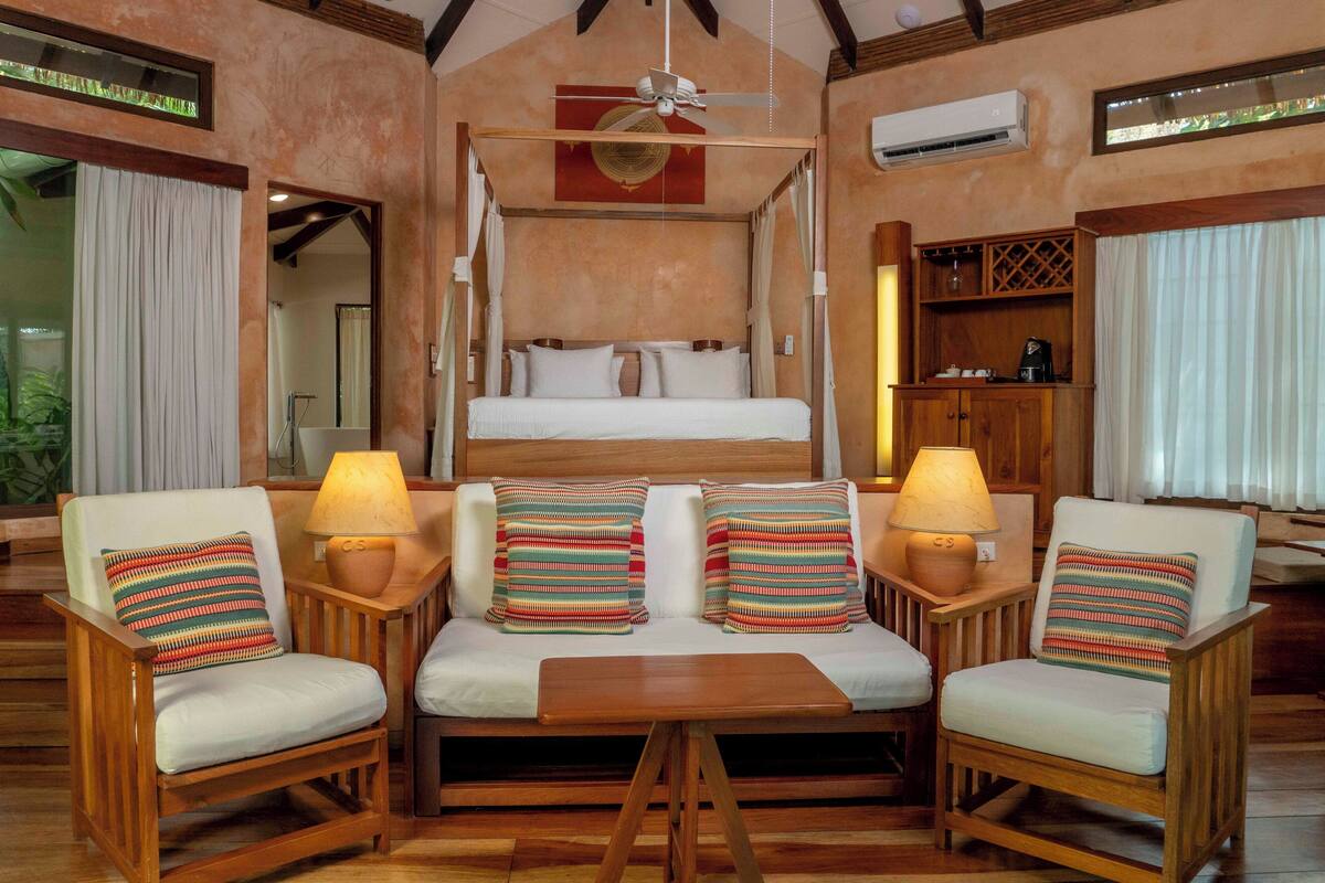 Un dormitorio con una cama con dosel, dos sillones con lámparas y una mesa de madera.