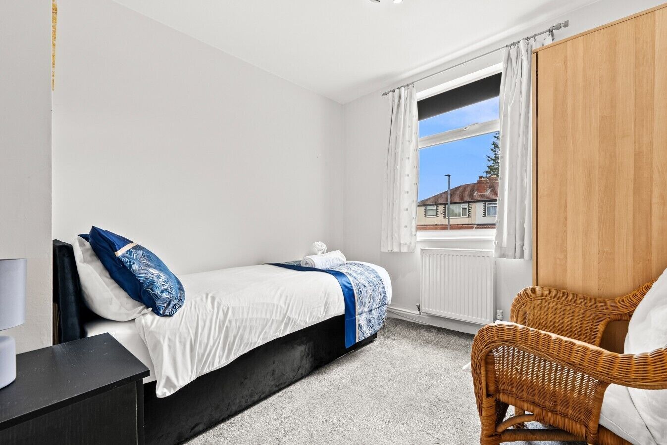 Une chambre à coucher avec un lit, une chaise, une fenêtre avec des rideaux et un radiateur.