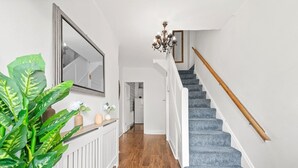 Un couloir avec un escalier, un miroir, un lustre et une plante.