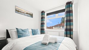 Un lit bien fait, avec une couverture bleue et blanche, un oreiller orné d’un motif de vagues bleues et une serviette posée sur le lit.