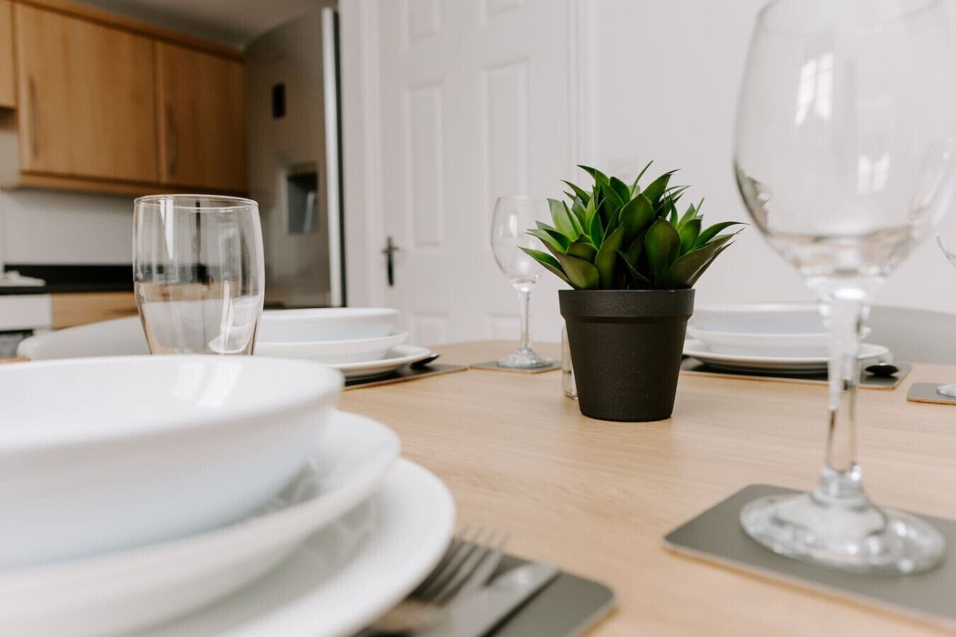 A dining table set with white plates, cutlery, and a potted plant.