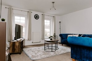 A living room with a blue sofa, a wooden TV stand, a round coffee table, and a patterned rug.