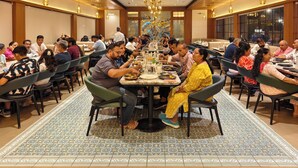 A dining area with multiple tables, chairs, and a chandelier. - ASHIRWAD CLUB RESORT (Jamnagar)