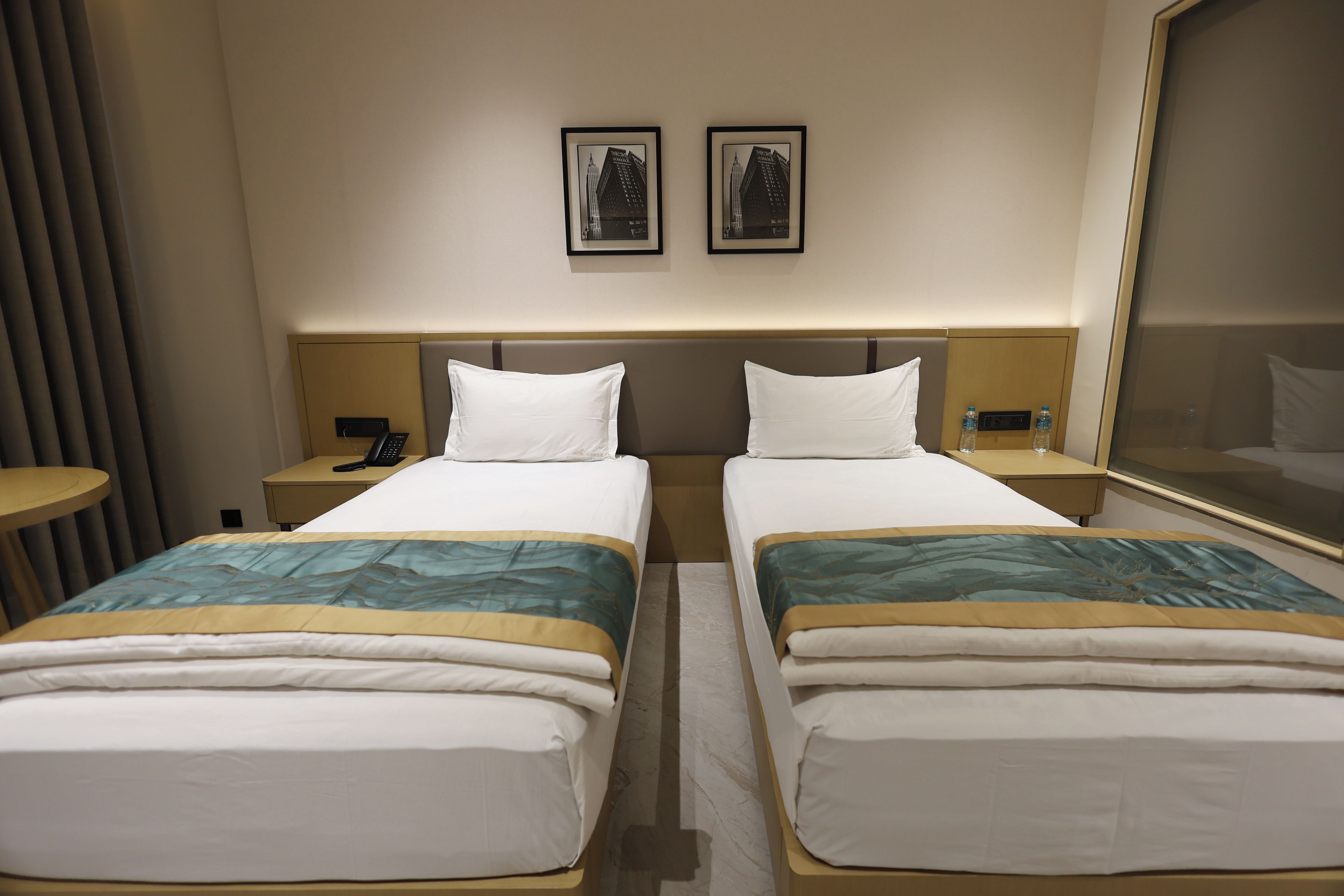 A hotel room with two beds, a bedside table with a phone, a mirror, and two framed pictures on the wall.