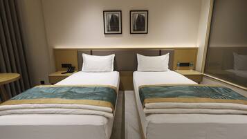 A hotel room with two beds, a bedside table with a phone, a mirror, and two framed pictures on the wall.