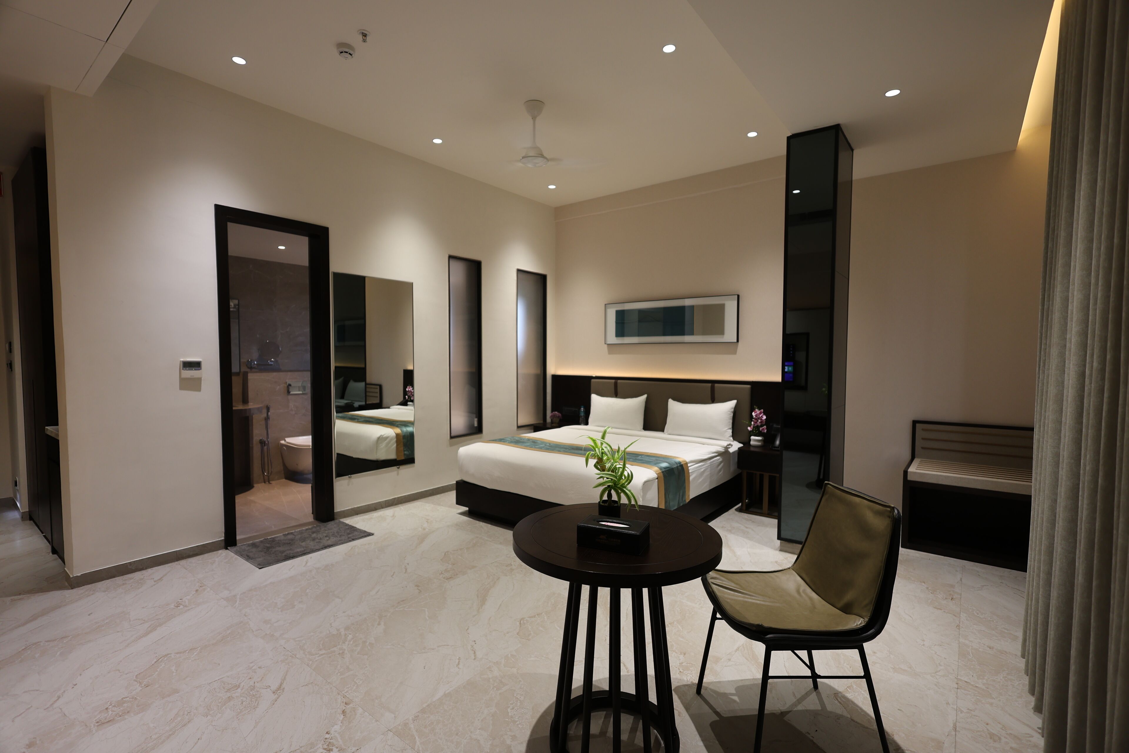 A modern hotel room with a bed, bedside table, chair, and a large mirror.
