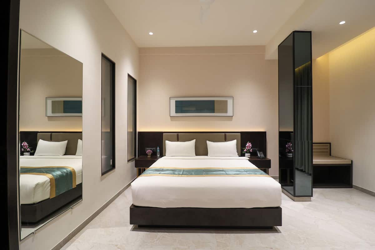 Quarto de hotel moderno com uma cama grande, mesa de cabeceira, espelho e um quadro na parede.