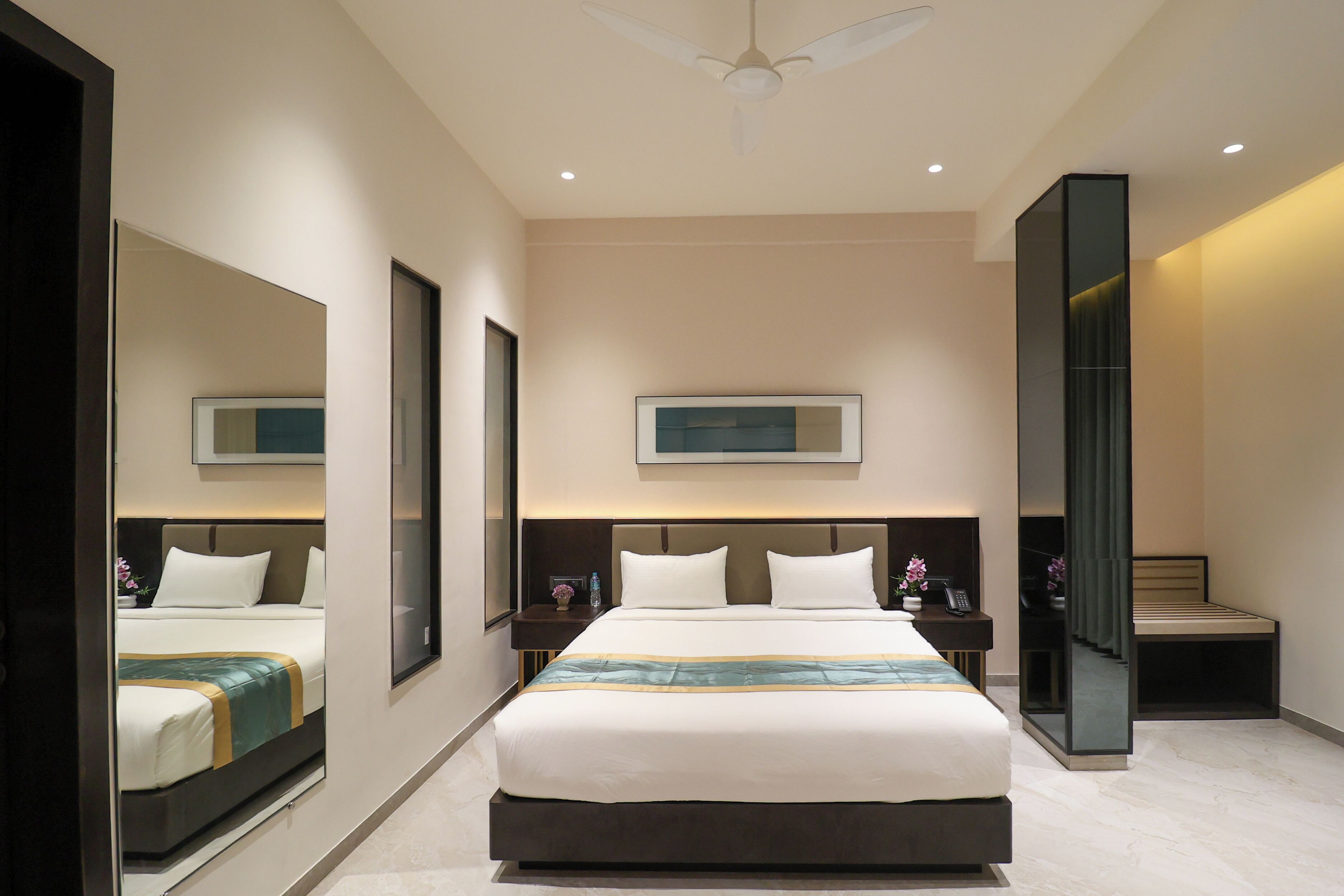 A modern hotel room with a large bed, bedside tables, a mirror, and a ceiling fan.