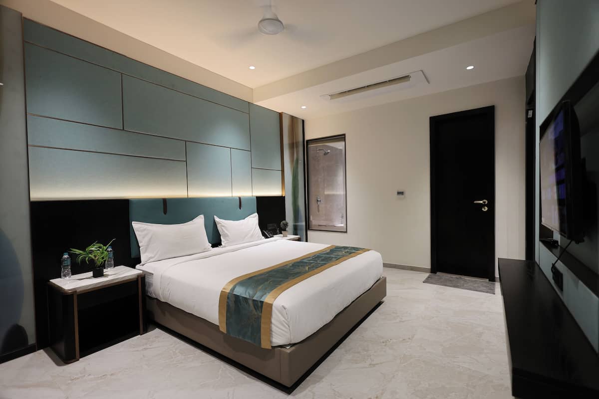 Quarto de hotel moderno com uma cama grande, uma mesinha de cabeceira com uma planta, uma televisão de tela plana e uma janela ampla.