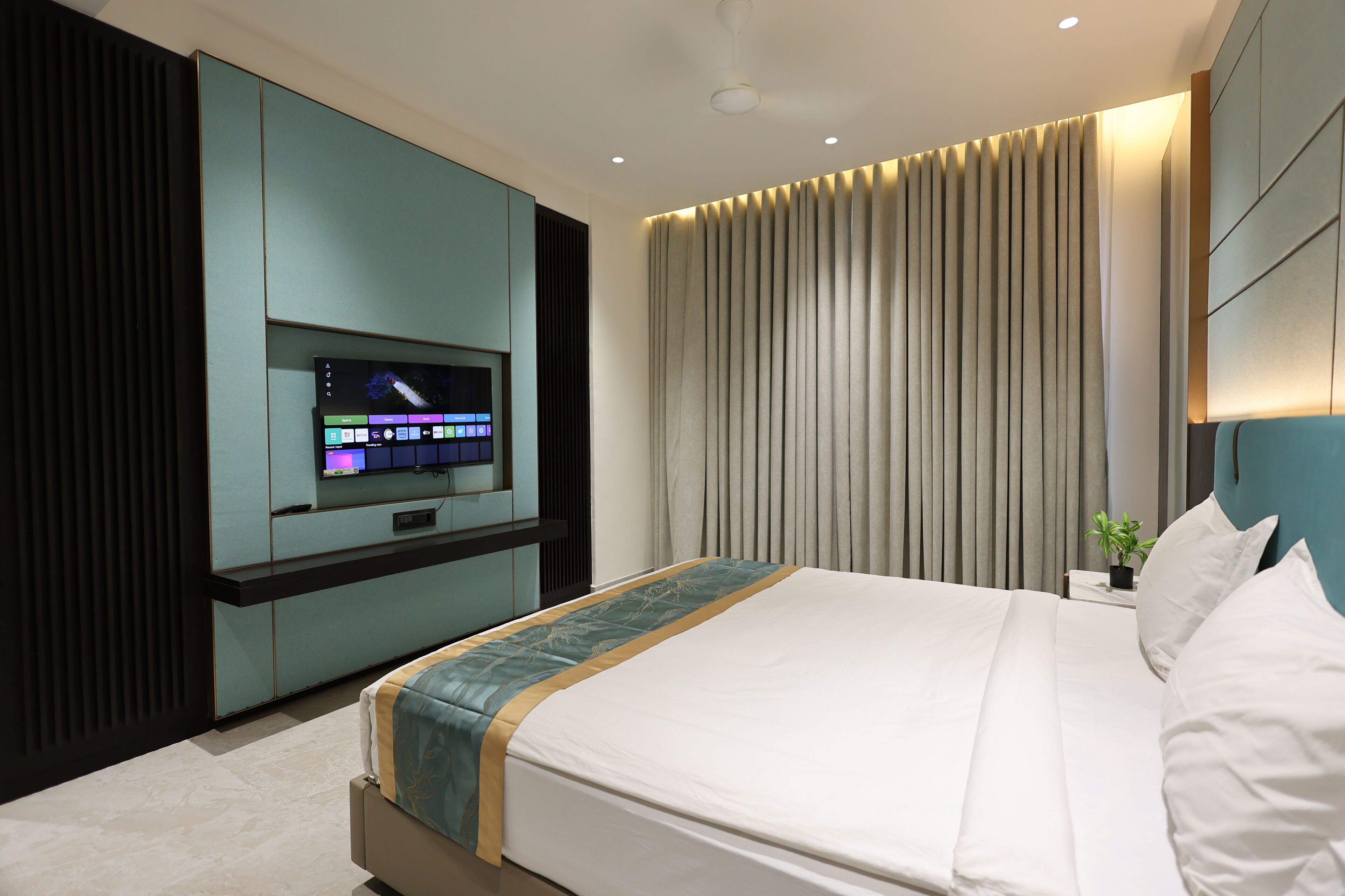 A modern hotel room with a large bed, a flat-screen TV mounted on a wall, and a large window with curtains.