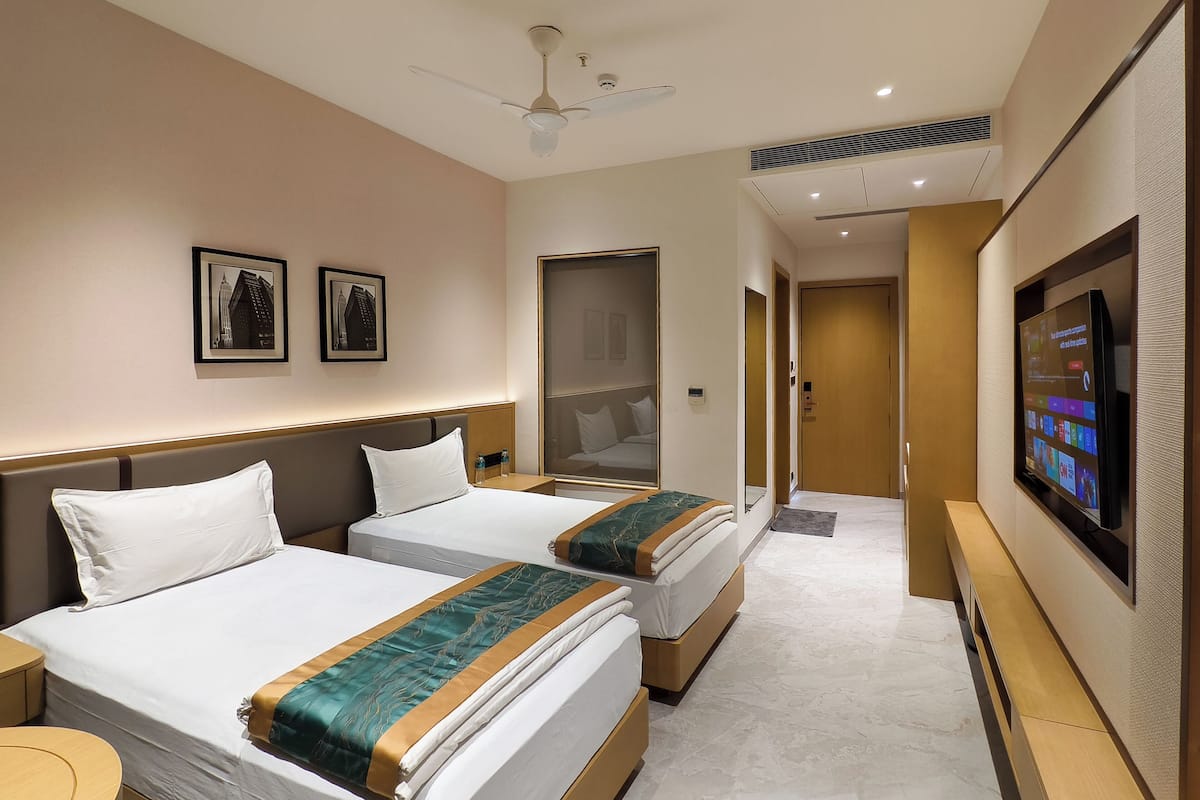 Quarto de hotel com duas camas, televisão, ventoinha no teto e quadros nas paredes.