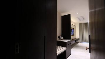 A modern hotel room with dark wood furniture, a flat-screen TV, a small seating area, and a large window with curtains.