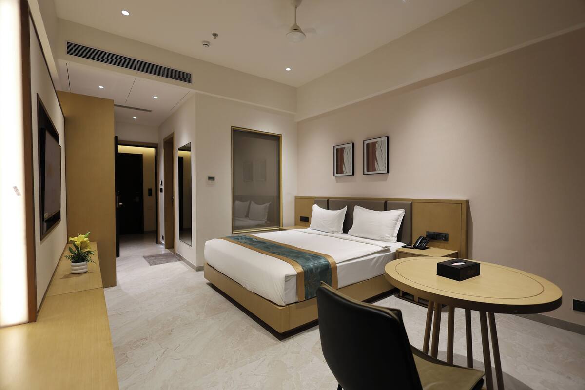 Quarto de hotel com cama, mesa de cabeceira, cadeira e uma mesinha redonda.
