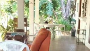 Un espacio exterior techado con una silla de plástico blanca, una silla naranja y una mesa.