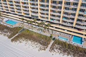 Un hotel de gran altura con varios balcones, una zona de piscina y vista al mar.