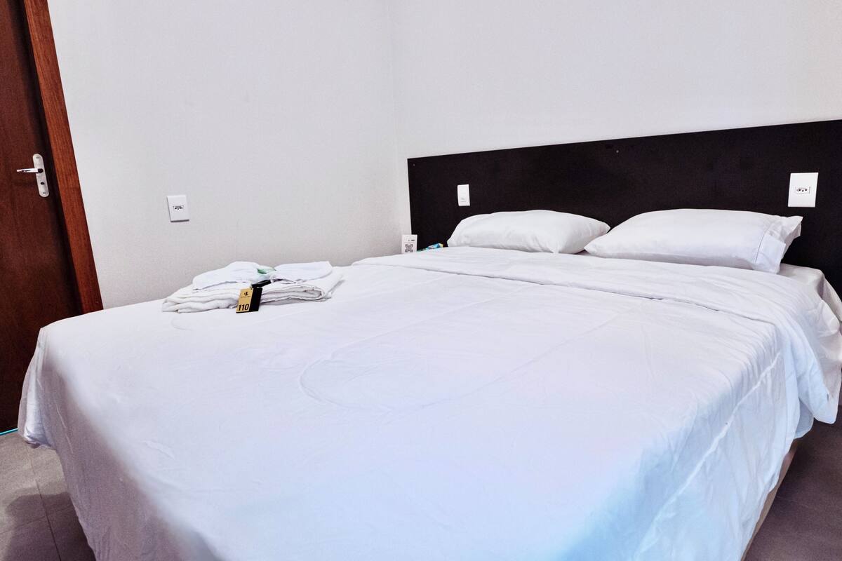 A neatly made bed with white linens, a wooden door frame, and a black headboard.