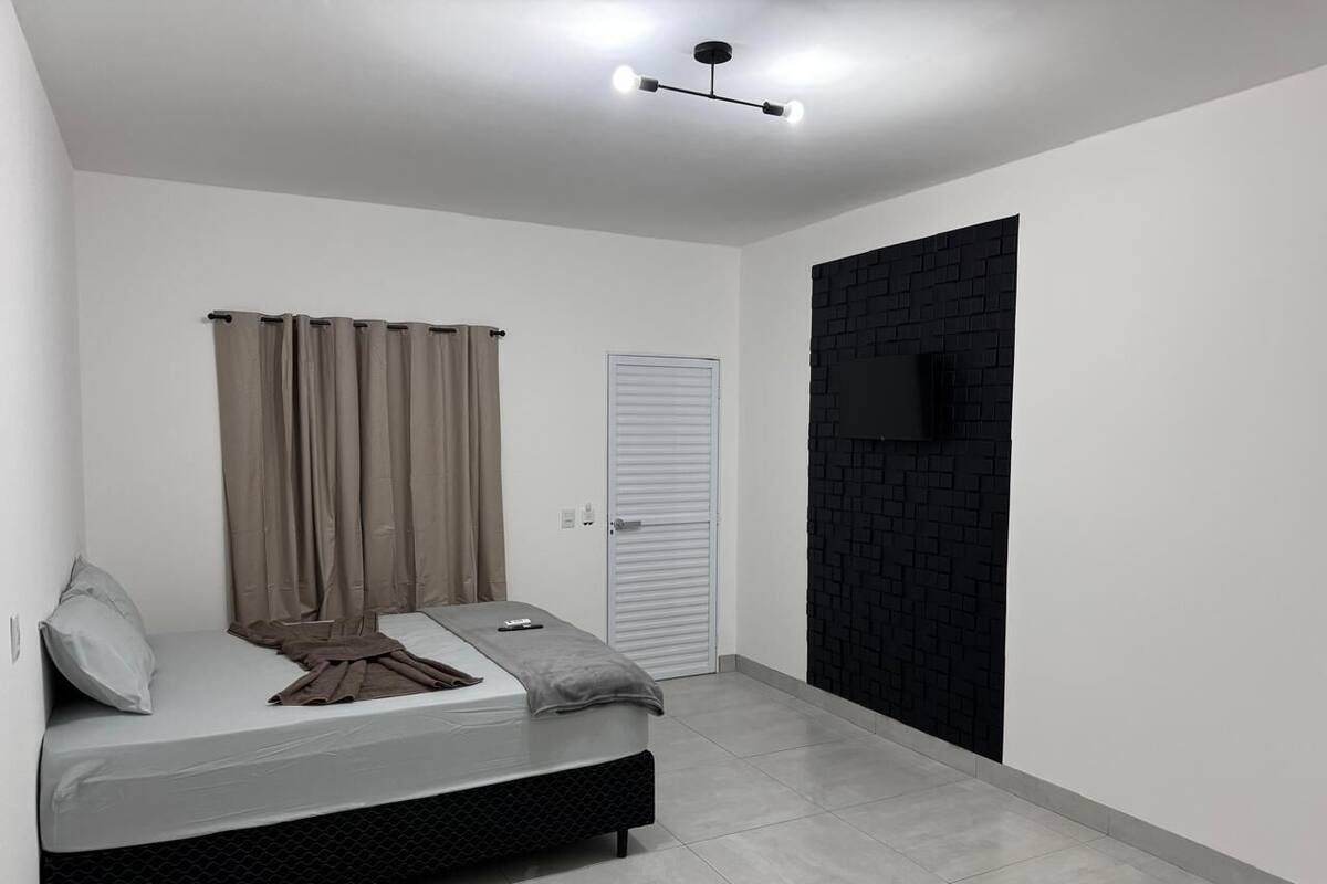 A bedroom with a bed, curtains, a television, and a door.