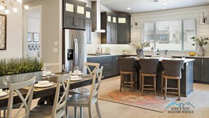 Una cocina moderna con armarios oscuros, una isla central con taburetes y una zona de comedor con mesa para cuatro.