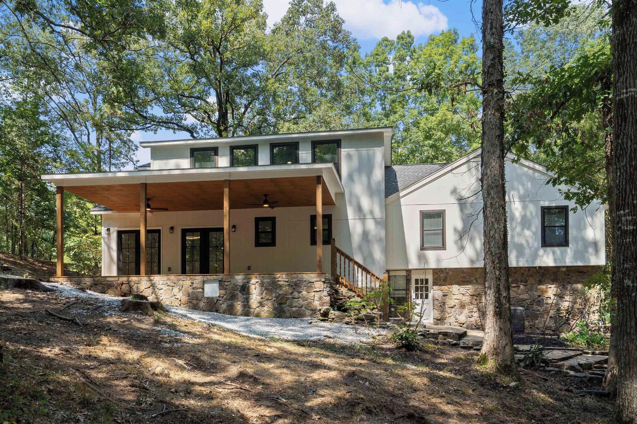 Une maison moderne à deux étages, dotée de fondations en pierre, de grandes fenêtres et d’un porche abrité.