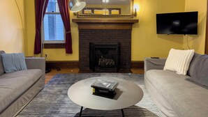 A living room with two sofas, a fireplace, a television, and a coffee table with books. - The Lodge (Sutton)