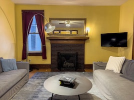 Una sala de estar con dos sofás, una chimenea, un televisor y una mesa de centro con libros.
