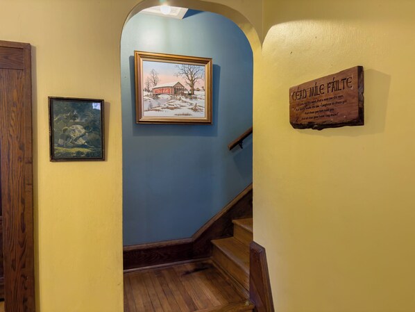 A hallway with a framed painting of a snowy landscape, a wooden sign with text, and a wooden staircase. - The Lodge (Sutton)
