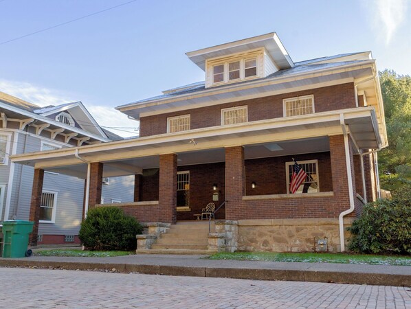 A two-story brick house with a covered porch, a small front yard, and an American flag.