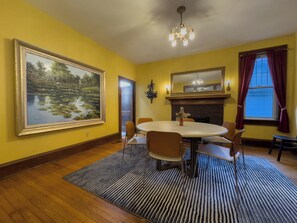 A dining room with a large landscape painting, a fireplace, and a chandelier.