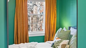A bedroom with teal walls, a bed with white bedding, a window with curtains, and a unique ceiling light fixture. - Old Town Living- Xcape to Vibrant Old Town (Alexandria)