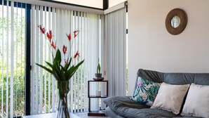 A modern living room with a grey sofa, a vase with red flowers, a small table, and a decorative mirror on the wall. - Villa 2 (2BR) w/Pool • Near Downtown Turrialba (Turrialba)