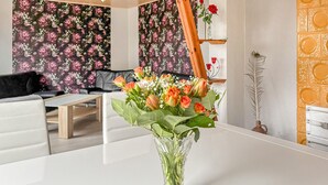 Un salon avec un canapé blanc, une table basse et un papier peint à motifs floraux. Un vase rempli de fleurs est posé sur une table.