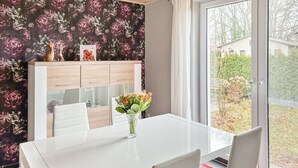 Un coin repas avec une table blanche, deux chaises, un vase de fleurs et un papier peint à motifs floraux.