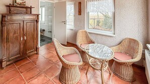 Une pièce chaleureuse, avec un meuble en bois, des chaises en osier, une petite table ronde et une fenêtre donnant sur l’extérieur.
