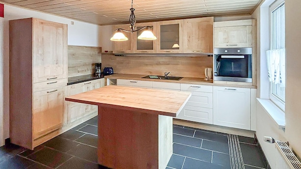 Une cuisine moderne dotée d’un îlot central, de meubles blancs, d’un four encastré et de luminaires suspendus.