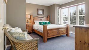 Une chambre à coucher avec un lit en bois, une chaise en osier, une table de chevet et une fenêtre avec des stores.