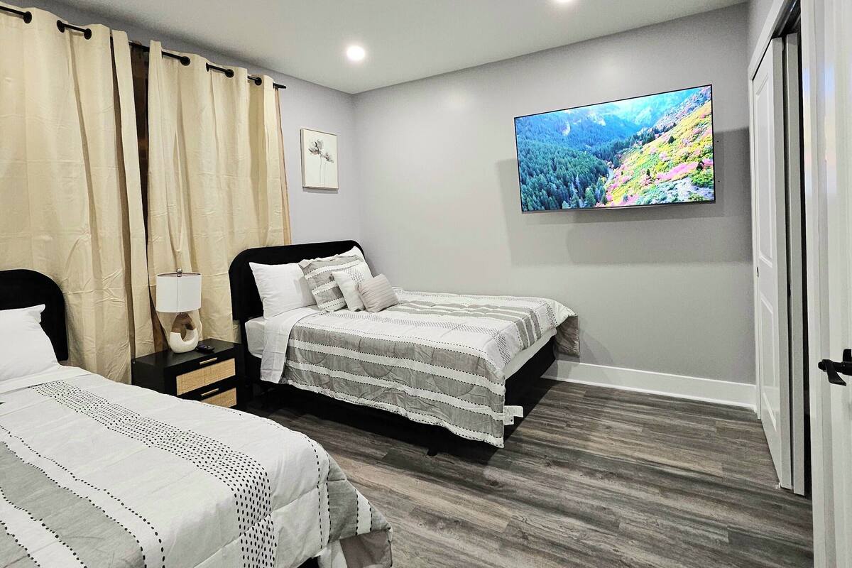 A bedroom with two beds, a TV on the wall, and a wooden floor.