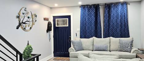 A modern living room with a sofa set, a staircase with a railing, and a decorative wall piece.