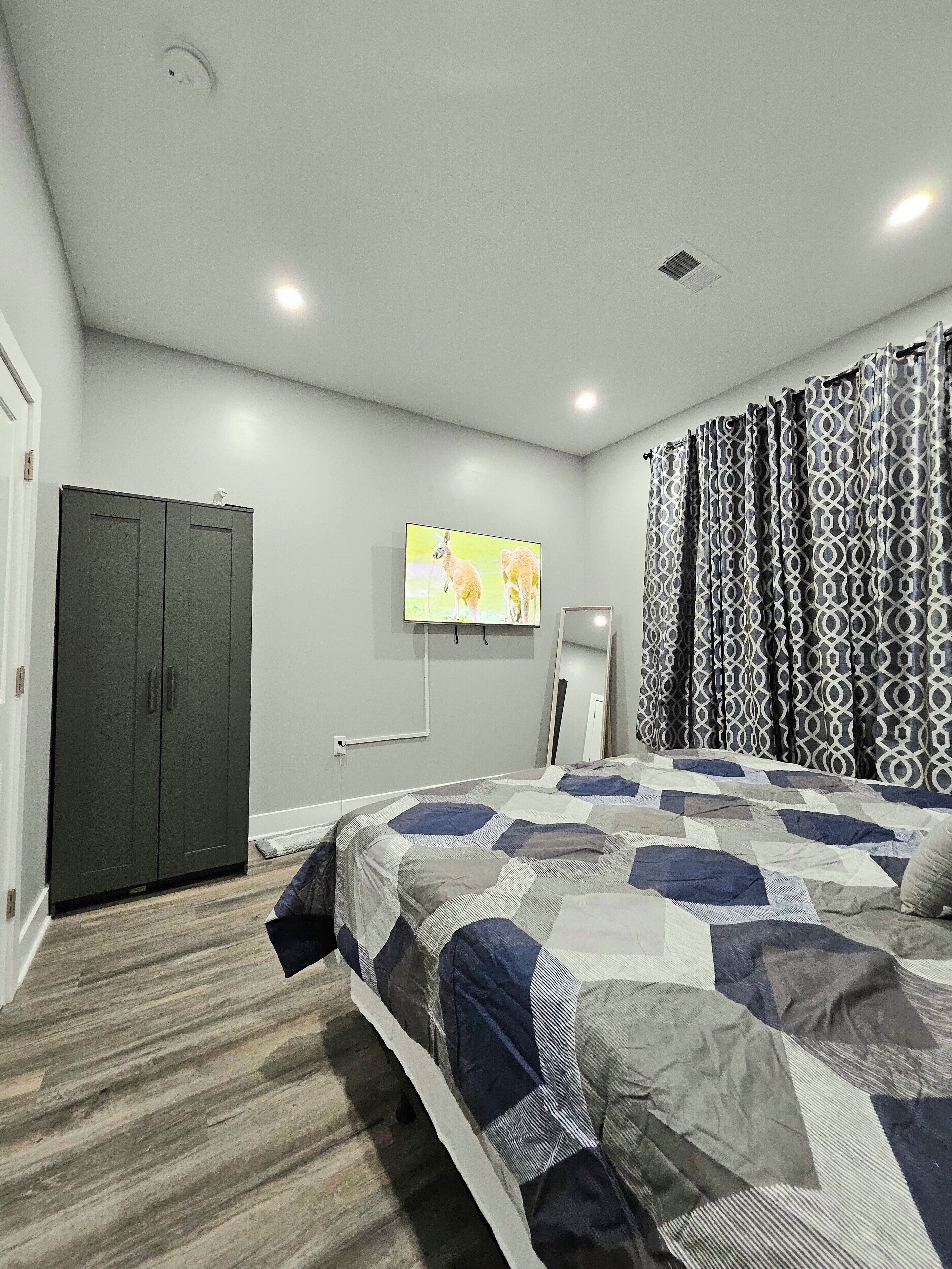 A bedroom with a bed, a wardrobe, a television, and patterned curtains.