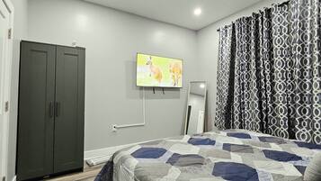 A bedroom with a bed, a wardrobe, a television, and patterned curtains.
