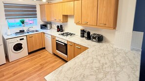 Une cuisine moderne avec des meubles en bois, un four encastré, un lave-linge et un plan de travail en marbre.