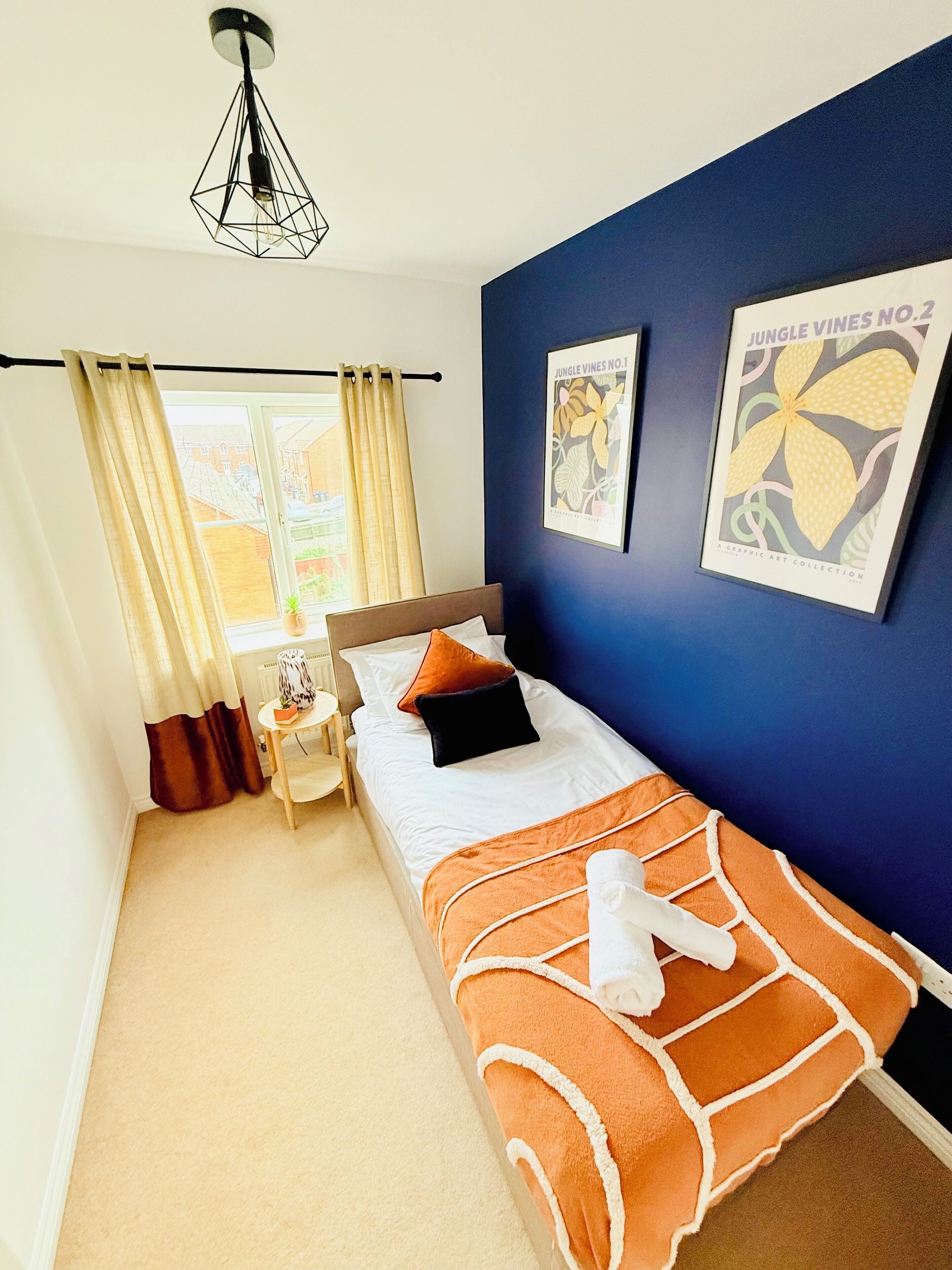 A bedroom with a bed, a nightstand, a lamp, and two framed posters on the wall.