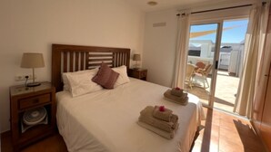 A hotel room with a bed, a nightstand, a lamp, a window with curtains, and a view of the outside. - Villa Las Coloradas - An Ideal Retreat in Playa Blanca (Playa Blanca)