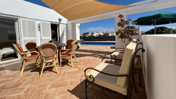 A terrace with wicker furniture, a table, and a view of the sea. - Villa Las Coloradas - An Ideal Retreat in Playa Blanca (Playa Blanca)
