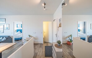 Ein modernes Hotelzimmer mit Holzboden, einem Bett mit blauer Bettwäsche, einem grauen Sofa und einem kleinen Tisch.