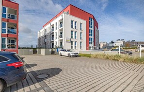 Ein mehrgeschossiges Gebäude mit rotem Dach und weißen Wänden, ein Parkplatz mit Autos und ein Schild für H&P Touristik.