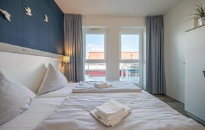 Ein Hotelzimmer mit zwei Betten, einem großen Fenster, Blickrichtung nach draußen und einer Pflanze an der Wand.