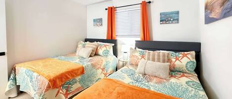 A room with two beds, each with a patterned bedspread and orange throw blankets.